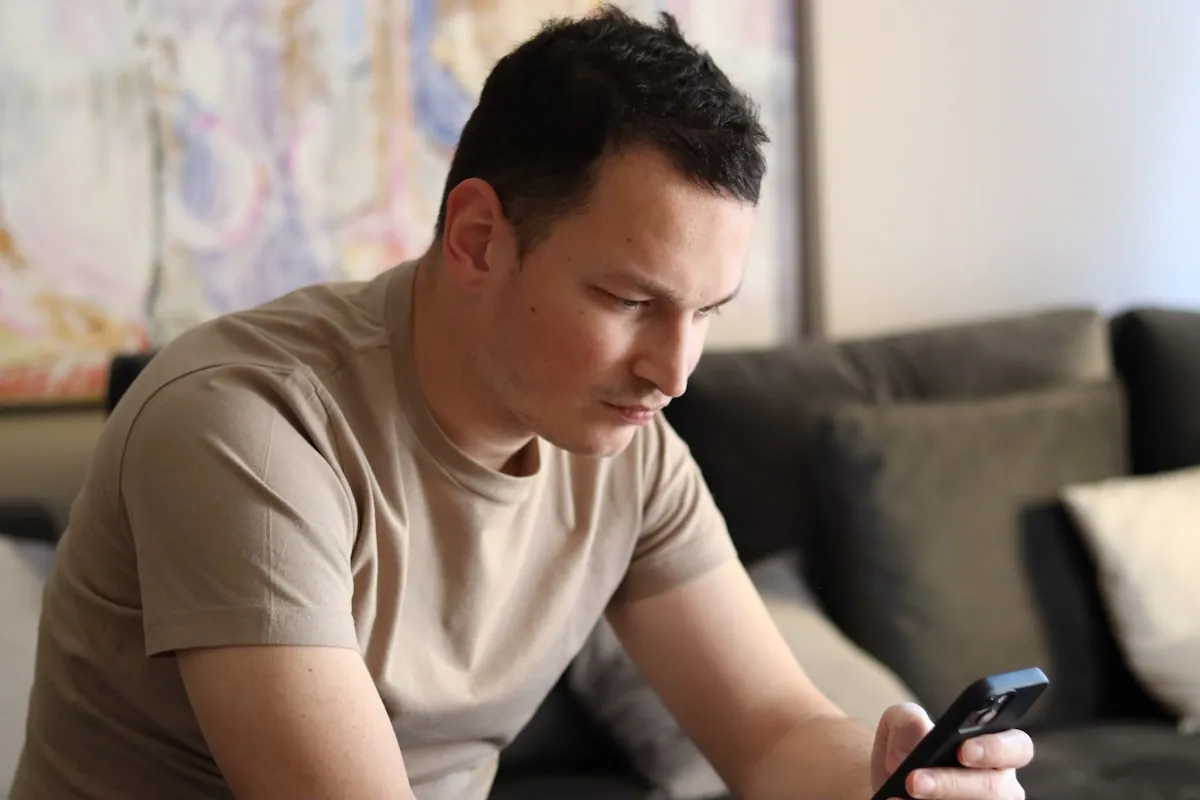 Person i sofaen som ser på mobilskjermen – nærbilde